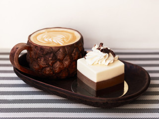 Freshly brewed cappuccino with latte-art in craft clay cup with sweet delicious chocolate dessert cake served in cozy trendy city cafe