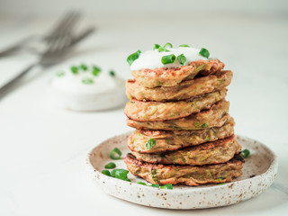 Zucchini fritters. Traditional zucchini fritters in stack on white background. Zucchini pancakes or fritters with green onion and parmesan cheese,served sour cream or greek yogurt. Copy space for text