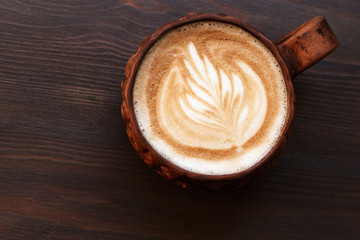 Freshly brewed cappuccino with latte-art in craft clay cup served on a dark wood table in trendy city cafe