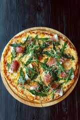 Pizza with bacon, cheese and herbs on a black wooden background