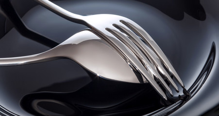 Empty plate with spoon and fork on a black background