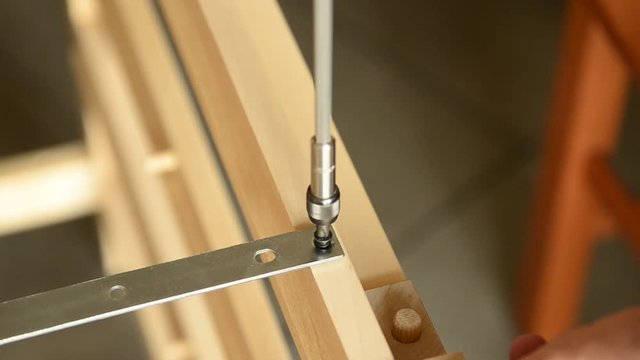 Close-up shot of a pair of screws that is fixed with an electric screwdriver on a light wooden board.