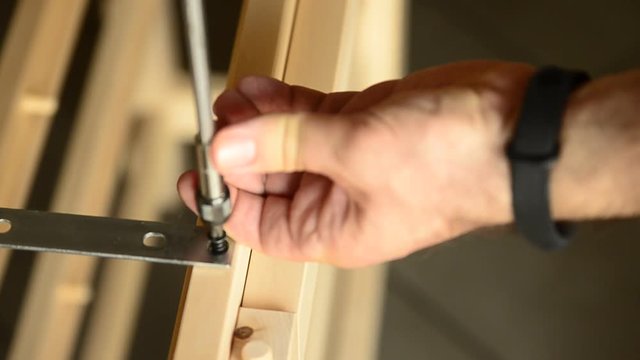 Close-up shot of a pair of screws that is fixed with an electric screwdriver on a light wooden board.