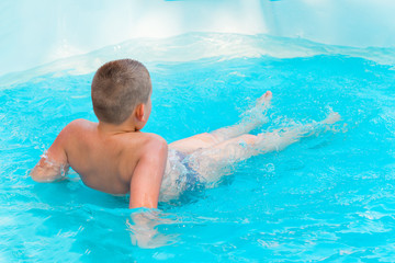 little cute boy swimming in the pool with turquoise water in the summer holidays