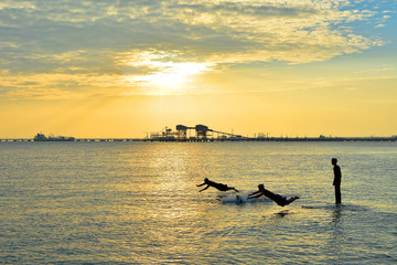 Silhouettes of young group of people swimming in ocean at sunset