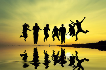 Fototapeta na wymiar Dramatic sky & reflections silhouette of happy people jumping over sunset, concept about having fun