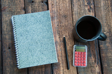 Gray notepad on the table. Next to a cup of coffee and a pen. On wooden background