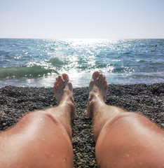 Men's feet on a pebble beach by the sea
