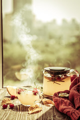 Autumn crunberry, rosemary and orange steaming tea in front of window, toned