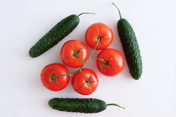 Five ripe red tomatoes on a branch and cucumbers on a white background. View from above.