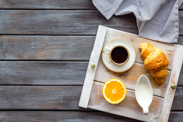 Breakfast on the tray with croissant, coffee with cream and fruit on wooden background top view mockup