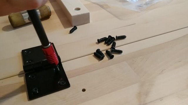 Fixing with a black metal hinge on two light wooden boards. The screwdriver is used for screwing. 30Fps