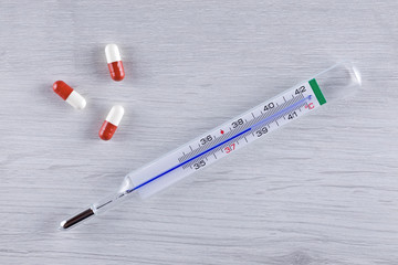 Pills and a medical thermometer showing a high temperature.