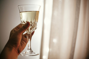Hand holding champagne glass on background of christmas lights, celebrating and toasting in festive room. Space for text. Happy New Year eve party. Happy Holidays