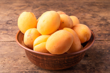Tasty ripe apricot berries in a clay bowl on a rustic wooden table close-up, top view, copy space