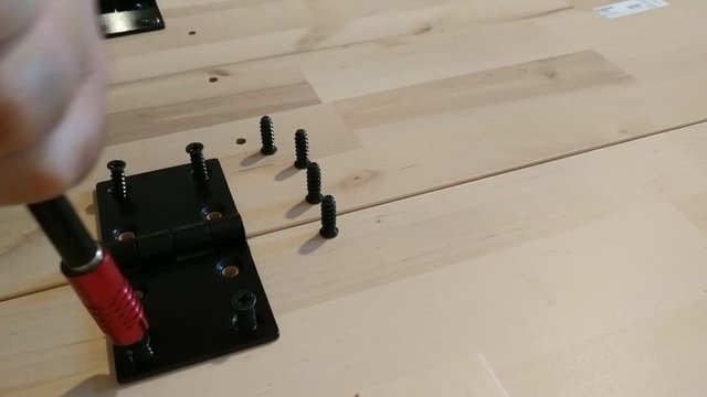 Fixing with a black metal hinge on two light wooden boards. The screwdriver is used for screwing. 25Fps