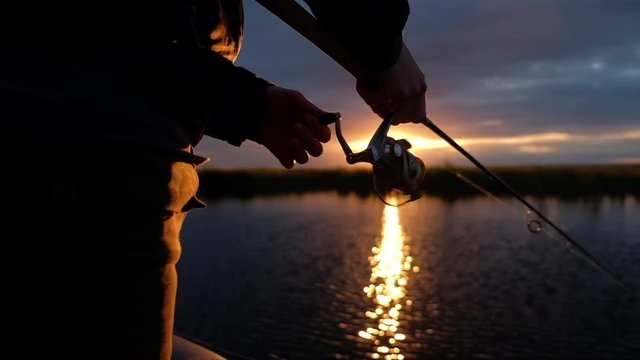 Fisherman spins the fishing reel on the lake at sunset