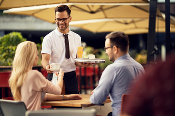 Smiling waiter serving coffee to a couple in a cafe.