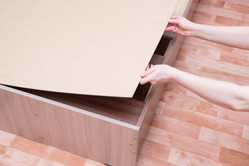 Assembling furniture. The Caucasian girl holds wooden flooring for the slatted bottom of the bed.