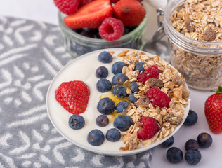 White yogurt in bowl with oatmeal and strawberries, blueberries and raspberries on the top on white background.