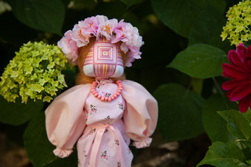 handmade motanka doll of pink color on a green background of flowers