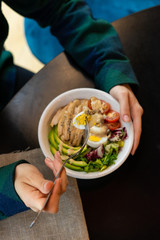 Woman is eating traditional american cobb salad with avocado, chicken breast, vinaigrette and hard boiled egg