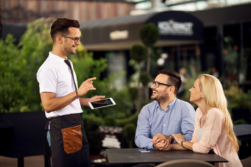 Happy waiter talking with a couple while taking their order in a cafe.