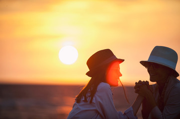 Silhouettes of two women together on the seaside at sunset