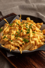 Mouthwatering hot french fries with a lot of cheese sauce with herbs in a pan, on a wooden board