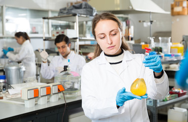 Female chemist analyzing liquid in test flasks