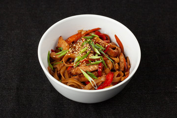 Wheat thick wok noodle with roasted bell pepper, soy sauce, chicken, carrot and sesame on black background