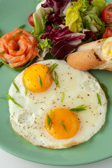 Top view of perfect fried couple of eggs with smoked salmon, mixed green salad and crunchy croutons with soft butter