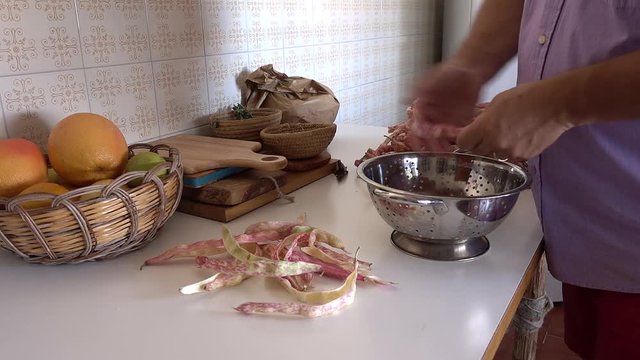 Human hands shelling fresh raw red kidney bean pods on table in the kitchen