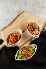 Different kinds of mac and cheese, served in portions on a wooden board: pasta with salmon and cucumber, pasta with meatballs and cheese, with chicken strips and tomatoes