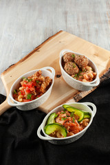 Different kinds of mac and cheese, served in portions on a wooden board: pasta with salmon and cucumber, pasta with meatballs and cheese, with chicken strips and tomatoes