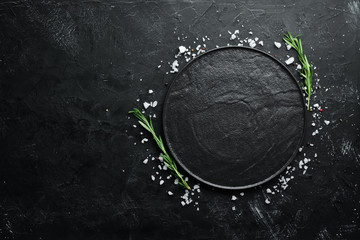 Black stone dish on a black background. Top view. Free space for your text. - obrazy, fototapety, plakaty