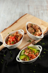 Different kinds of mac and cheese, served in portions on a wooden board: pasta with salmon and cucumber, pasta with meatballs and cheese, with chicken strips and tomatoes