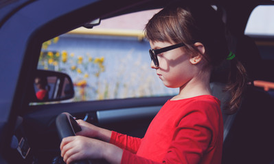 Driving shool. Humorous photo of cute little child girl holds a wheel in a car and learns to drive.