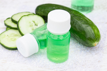 Sliced cucumber and a bottle of cucumber extract on a white wooden table and a white background. Liquid cosmetics for skin care.
