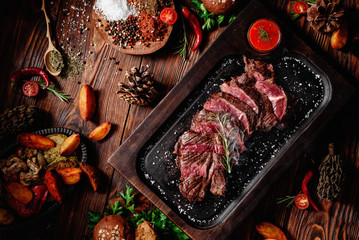 Juicy roasted veal tenderloin sliced decorated rosemary on dark board on dark wooden background in beautiful composition among vegetables and spices. Top view. Flat lay - obrazy, fototapety, plakaty