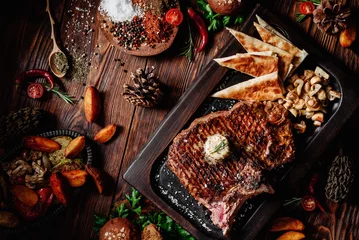 Foto auf Acrylglas Juicy grilled steak T-Bone decorated rosemary on dark board with mushrooms and fried pita bread on dark wooden background in beautiful composition among vegetables and spices. Top view. Flat lay © Kirill