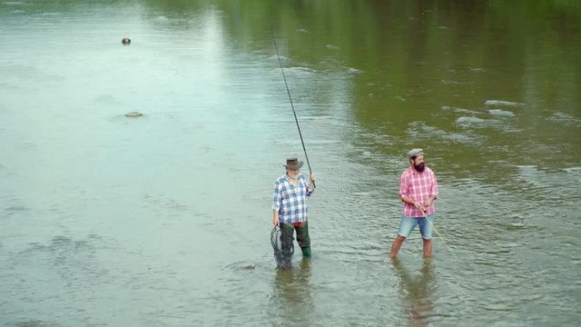 Father and son ishing. Fly rod and reel with a brown trout from a stream. Happy father and son together fishing in summer day under beautiful sky on the river. Fly fishing.