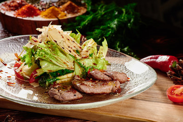 Roasted meat slices and Salad with fresh vegetables and parmesan in transparent plate on wooden background in beautiful composition among vegetables and spices. Top view. Flat lay