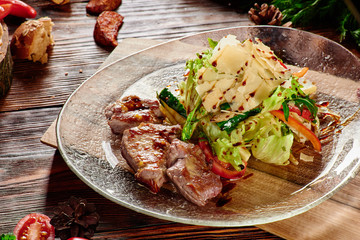 Roasted meat slices and Salad with fresh vegetables and parmesan in transparent plate on wooden background in beautiful composition among vegetables and spices. Top view. Flat lay