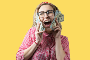 Closeup of young beautiful woman in a red plaid shirt in glasses with american dollars money in hand over yellow background.	
