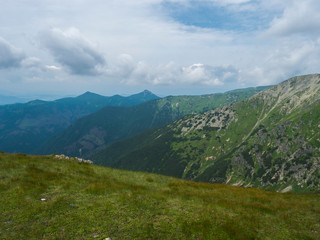 Fototapeta premium Piękny górski krajobraz z bujną zieloną trawą, łąką i nagimi szczytami górskimi na grzbiecie Tatr Zachodnich, Rohacze Słowacja, lato dramatyczne chmury na tle nieba
