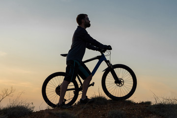 Naklejka na ściany i meble Cyclist in shorts and jersey on a modern carbon hardtail bike with an air suspension fork rides off-road on the orange-red hills at sunset evening in summer 
