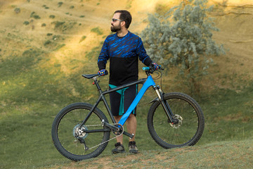 Cyclist in shorts and jersey on a modern carbon hardtail bike with an air suspension fork rides off-road on the orange-red hills at sunset evening in summer	