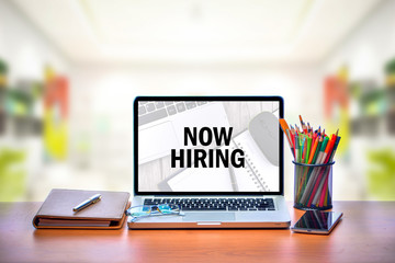 Open laptop with isolated white screen on old wooden desk with text NOW HIRING