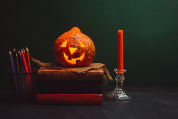 Halloween pumpkin on a pile of books next to a burning candle